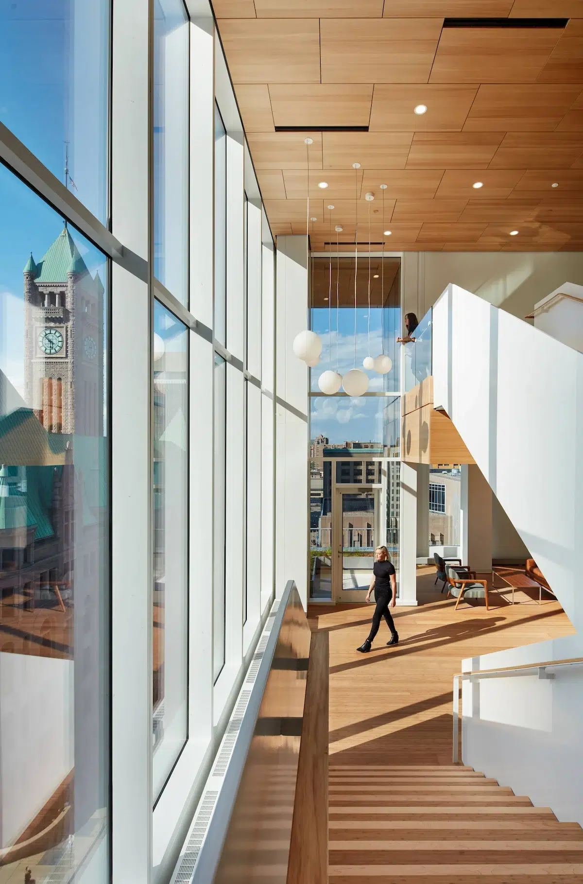 A woman walks between staircases in a modern building with lots of natural light and a view of the Minneapolis City Hall.