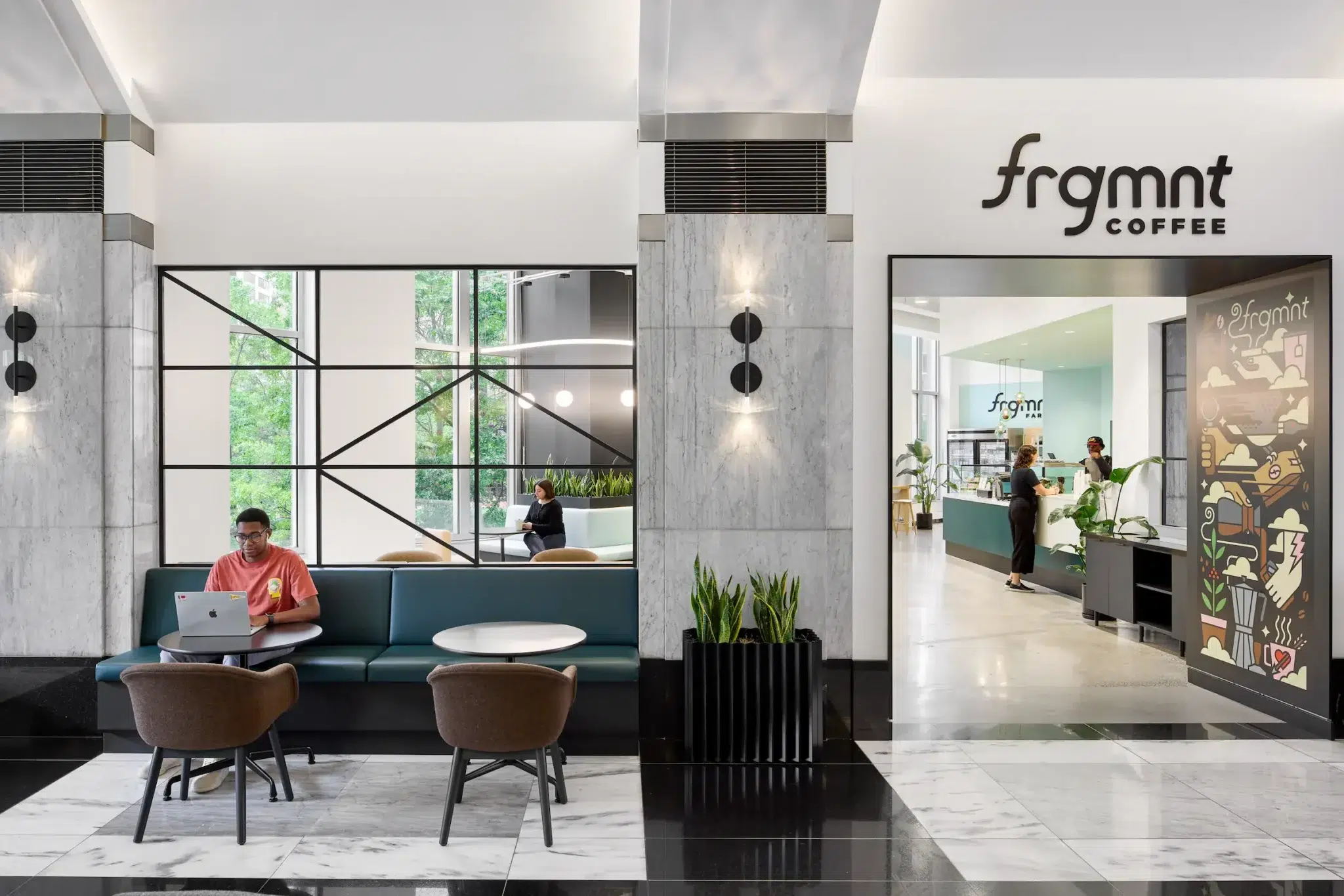 A man works on a laptop outside an on-site cafe in a sleek modern office. 