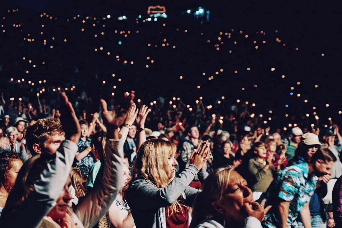 Crowd at a concert, with people holding up lit devices, creating a sea of lights in the darkened venue.