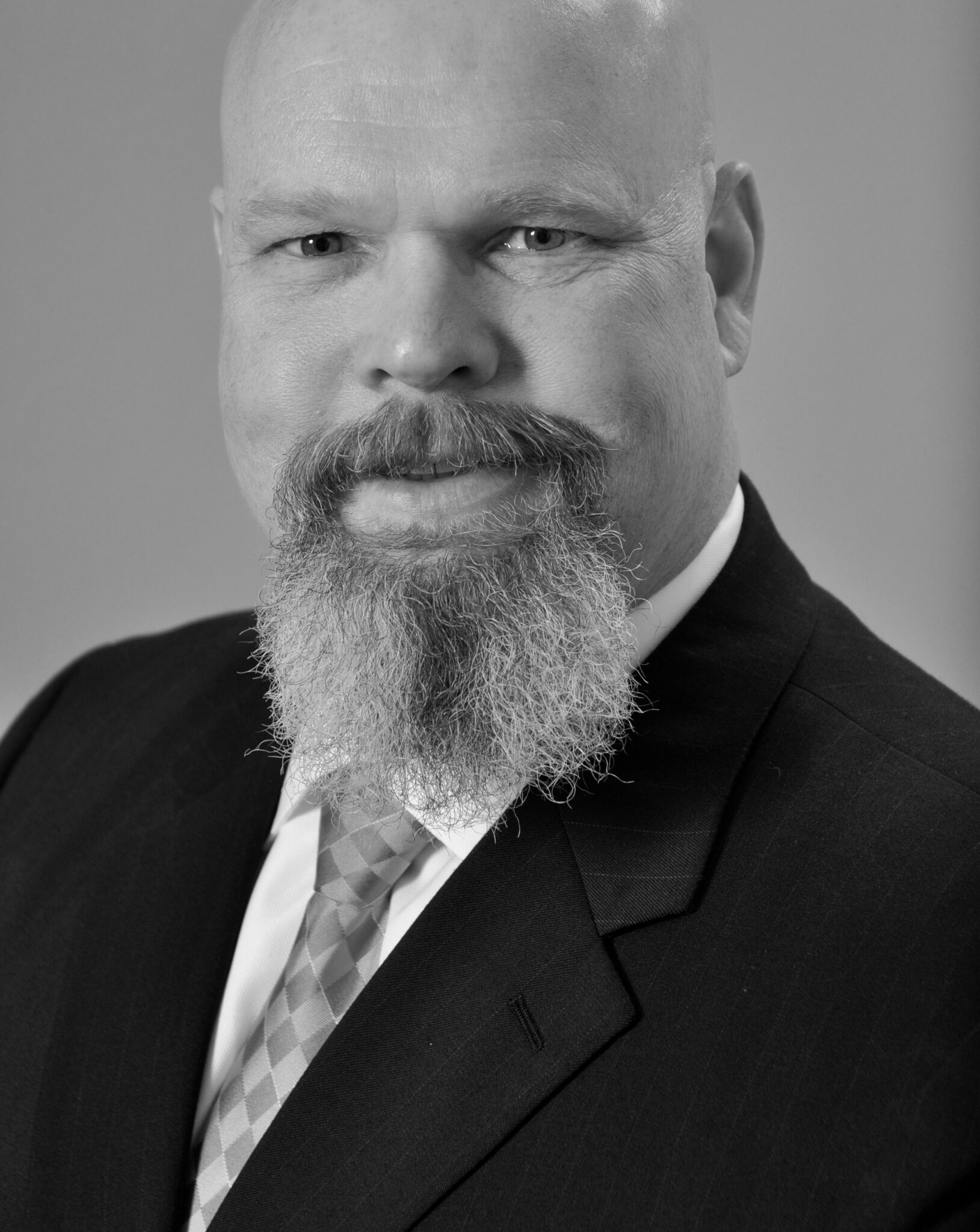 A bald man with a beard wearing a suit and tie, looking at the camera, in a black and white portrait.