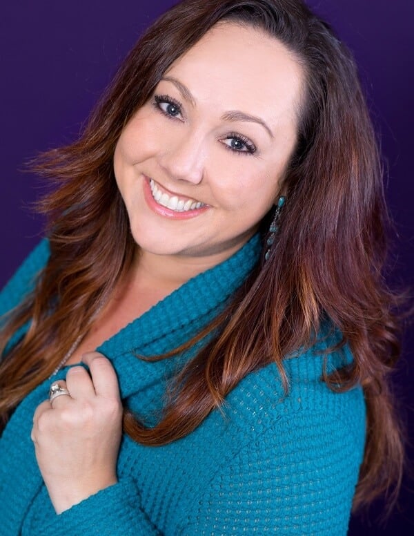 Smiling woman with long brown hair, wearing a teal sweater, against a purple background.