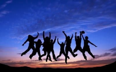 Silhouettes of people jumping joyfully against a twilight sky with scattered clouds.