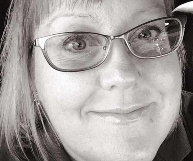 Woman with glasses, smiling, in a close-up black and white photo.