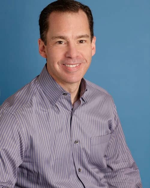 Smiling man wearing a striped shirt against a blue background.