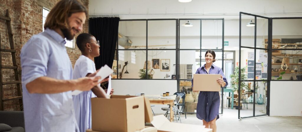 A woman carrying a box through a modern office surrounded by colleagues