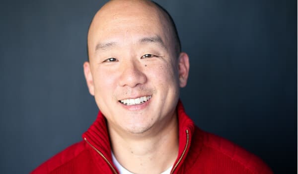 Smiling person in a red sweater against a dark background.