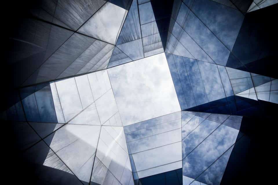 Geometric glass ceiling with sky visible through angular, reflective panels.