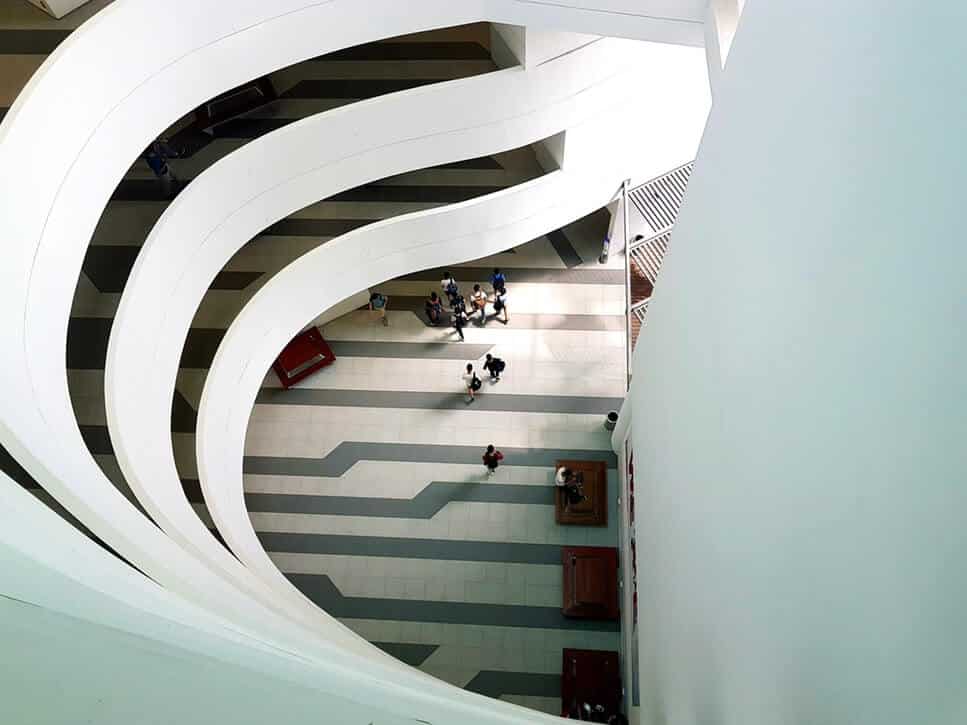 White spiral staircase inside a modern building, with people gathered on the ground floor below.