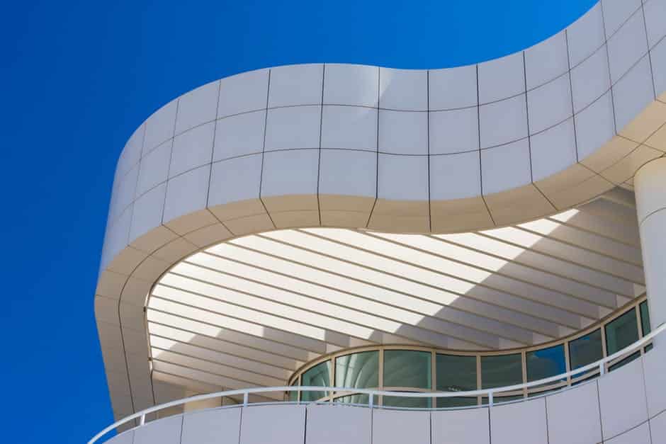 Curved modern building facade with white panels against a clear blue sky.