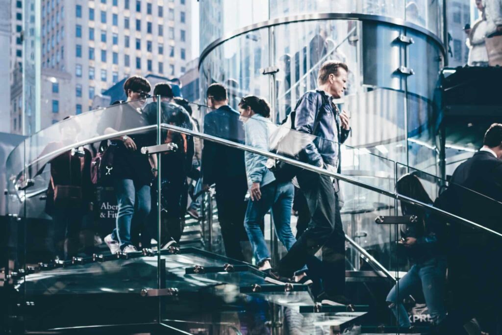 People walking on a modern glass staircase in an urban setting with tall buildings in the background.