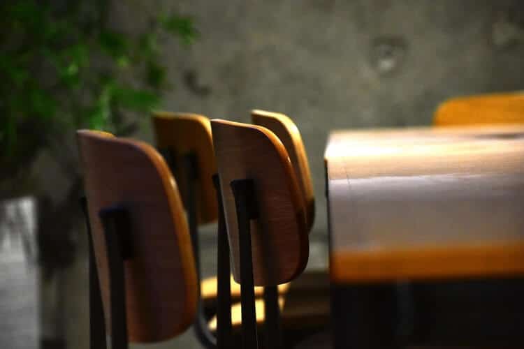 Wooden chairs lined up at a table with a plant in the background.