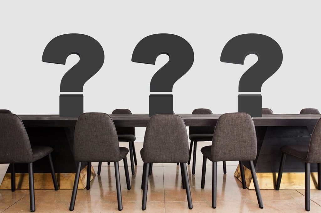 Meeting room with a long table and chairs, three large question marks on the table.