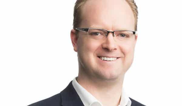 Smiling person with glasses wearing a suit against a white background.