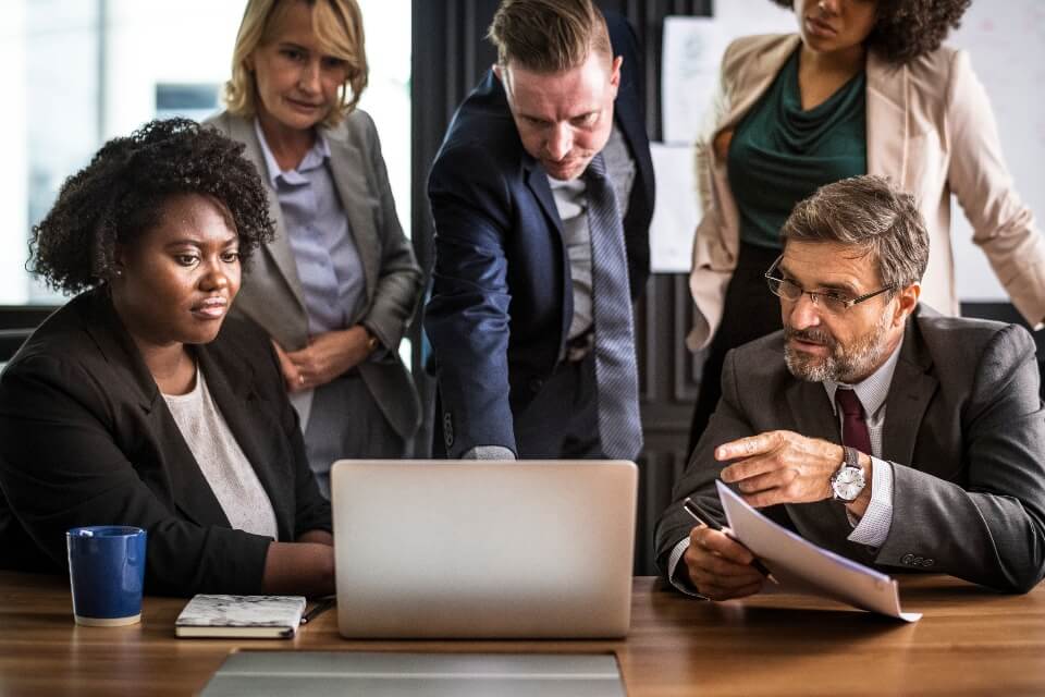 A diverse group of professionals discussing a project around a laptop at a conference table.