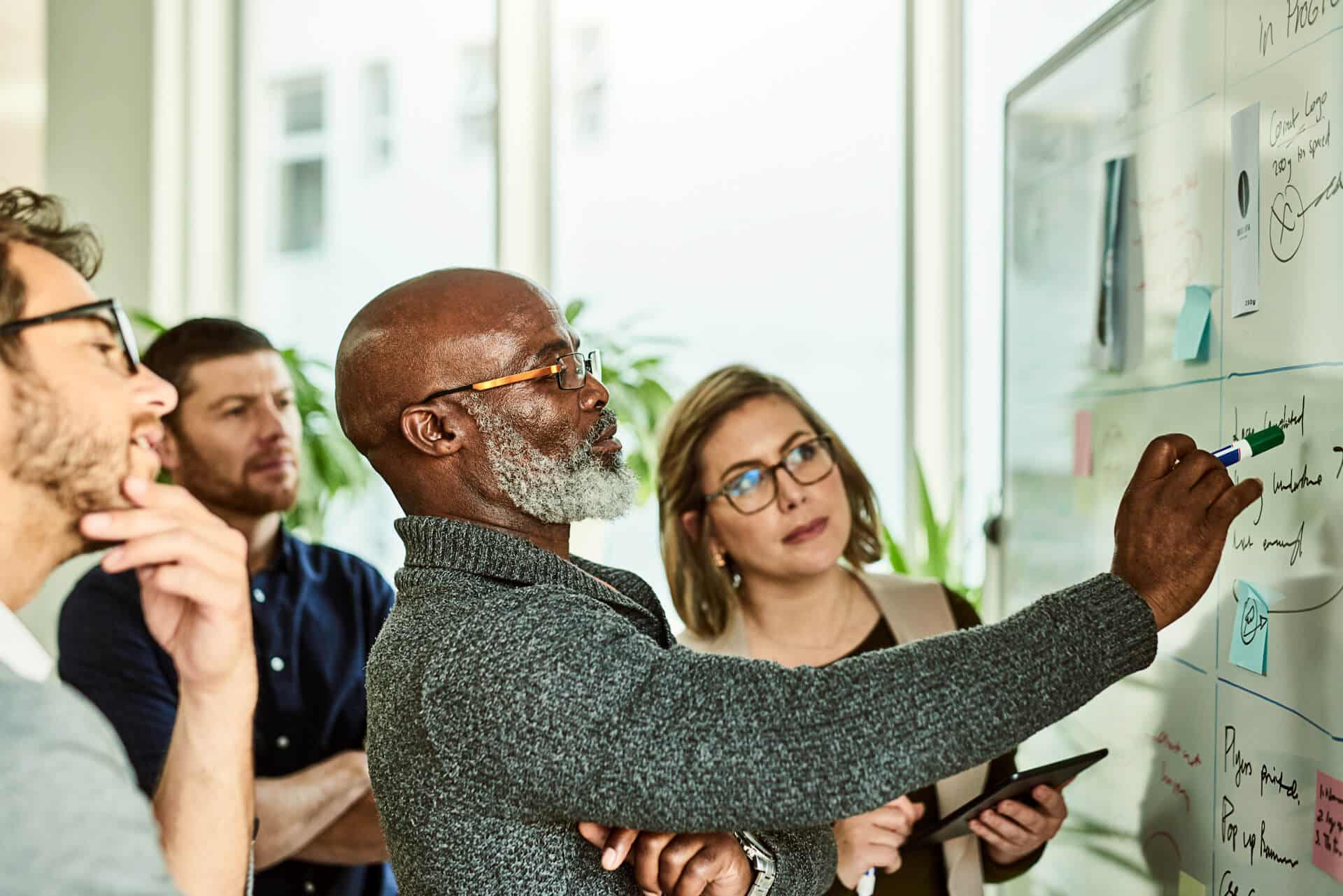 A group of people discussing and writing on a whiteboard in an office setting.