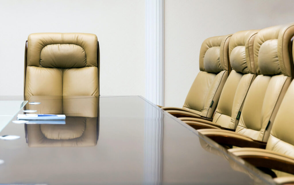 Empty conference room with a long glass table and beige leather chairs arranged around it.