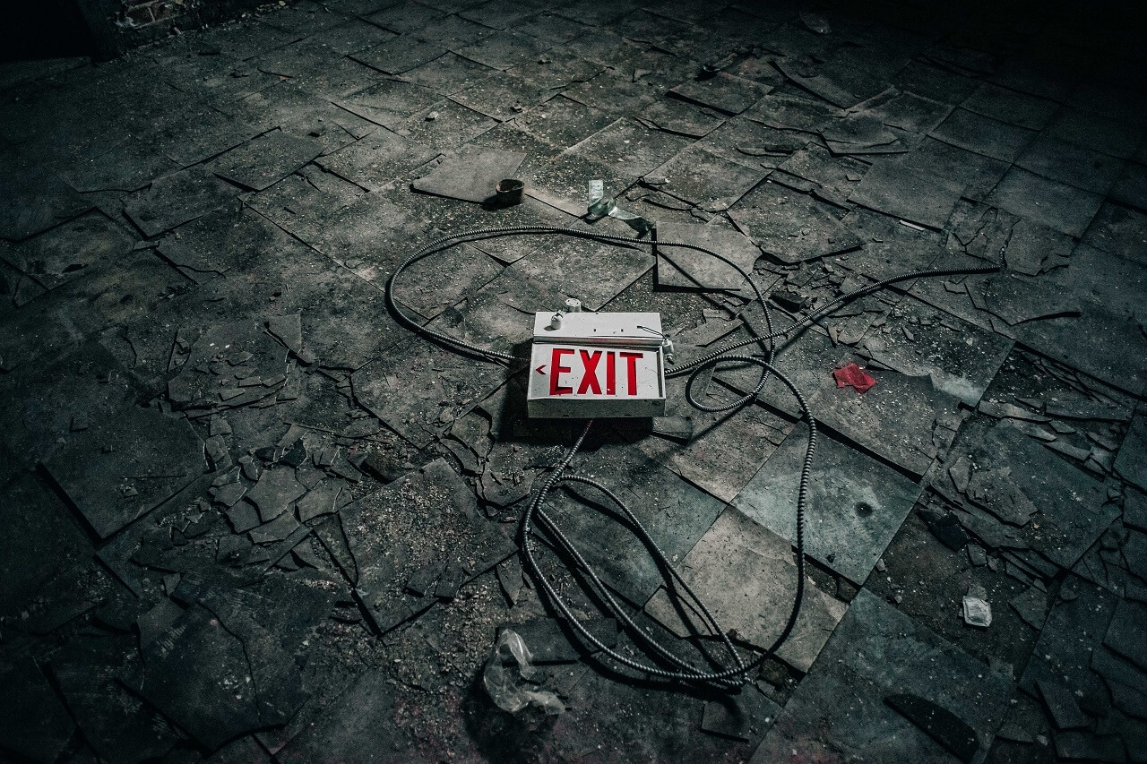 A broken "EXIT" sign lies on a cracked, dirty floor with scattered debris and wires.