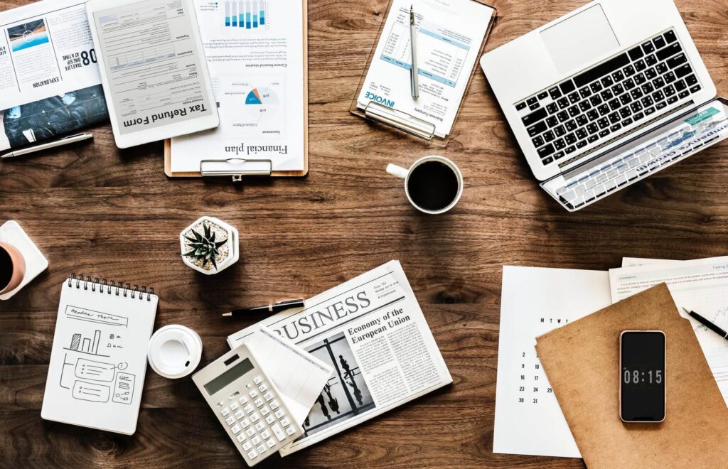 Office desk with a laptop, coffee, documents, calculator, and a smartphone displaying 08:15.