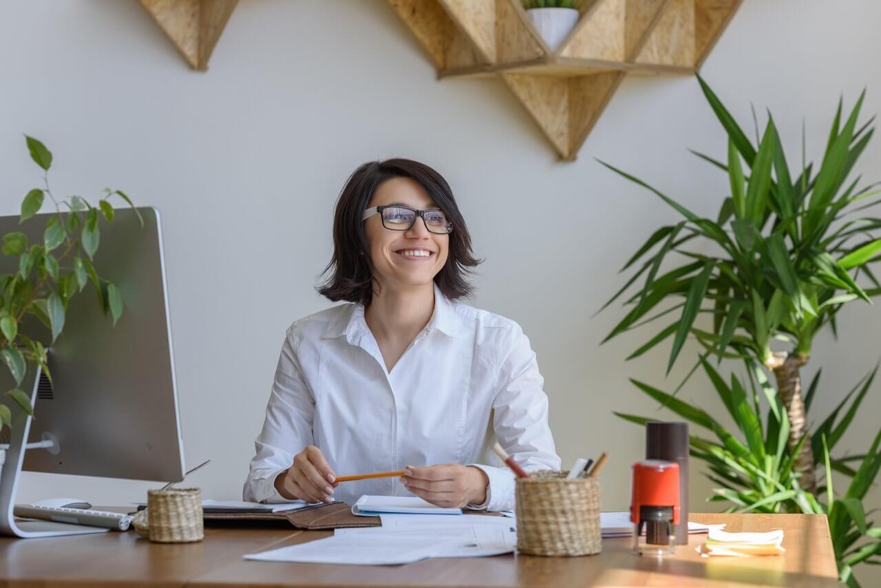 Woman Smiling Sitting at Desk with Plants