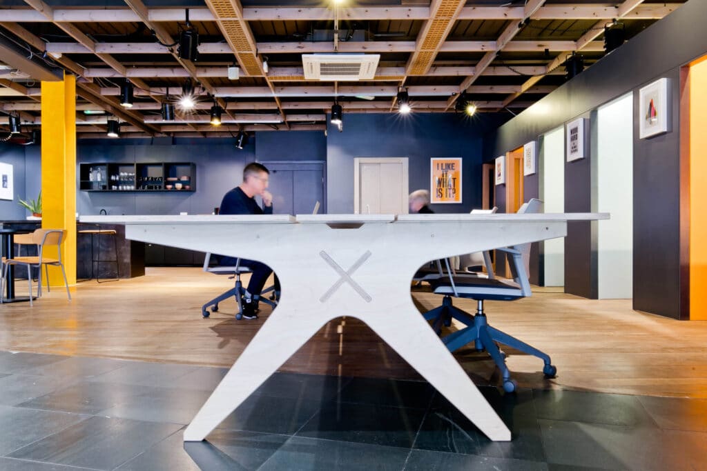 Modern office space with a large table, two people sitting, and colorful walls in the background.