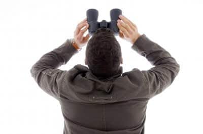 Person looking up through binoculars against a white background.