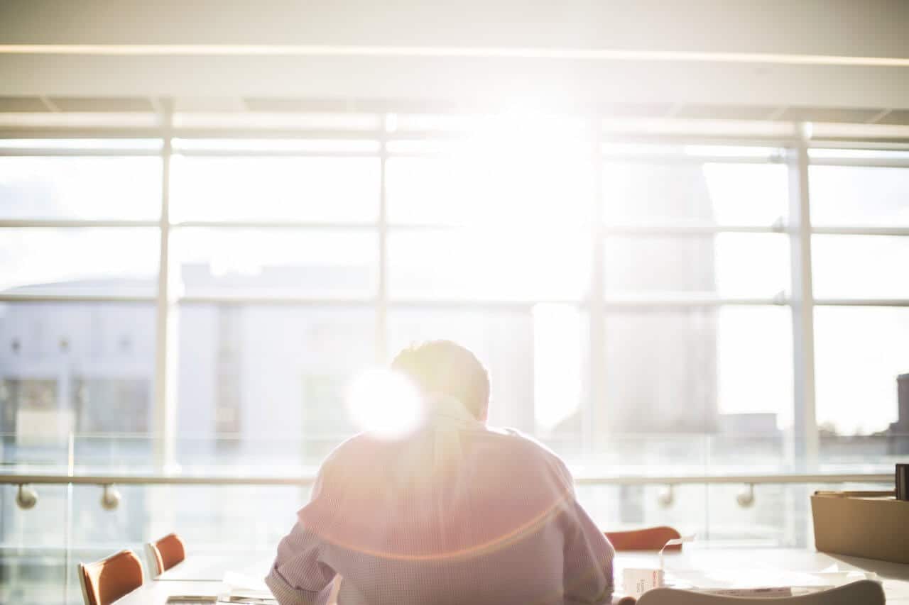 Person sitting at a desk in a sunlit office, large windows showing blurred buildings outside.