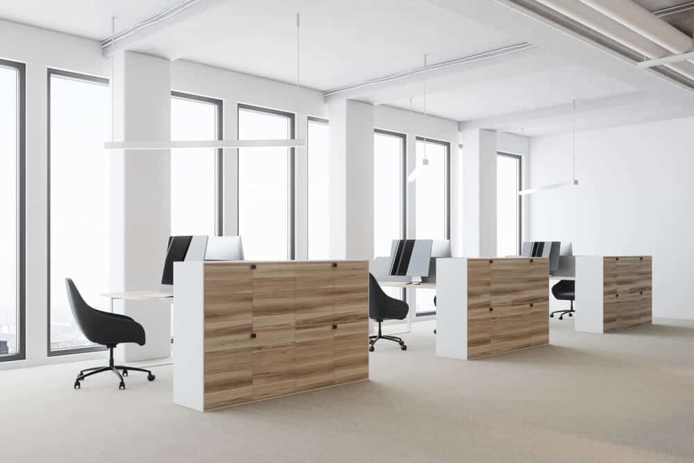 Modern office with wooden desks, black chairs, and large windows letting in natural light.