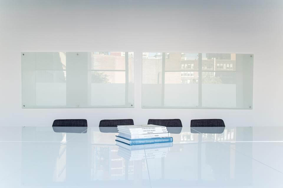 Minimalist conference room with a glossy table, stack of books, dark chairs, and large windows.