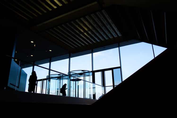 Silhouettes of people in a modern building with large windows and revolving doors.