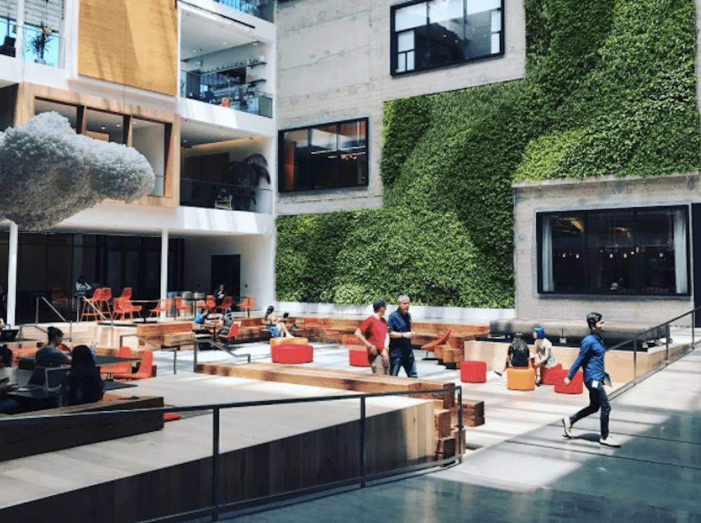 Modern indoor atrium with green wall, seating areas, and people walking and sitting.