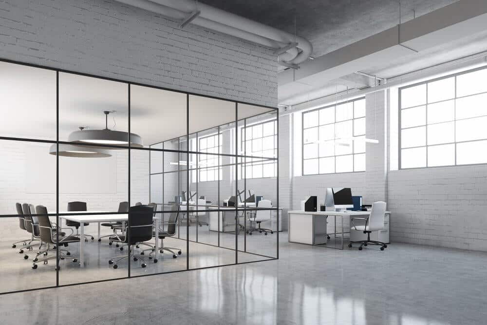 Modern open-plan office with glass-walled meeting room, desks, computers, white walls, and large windows.