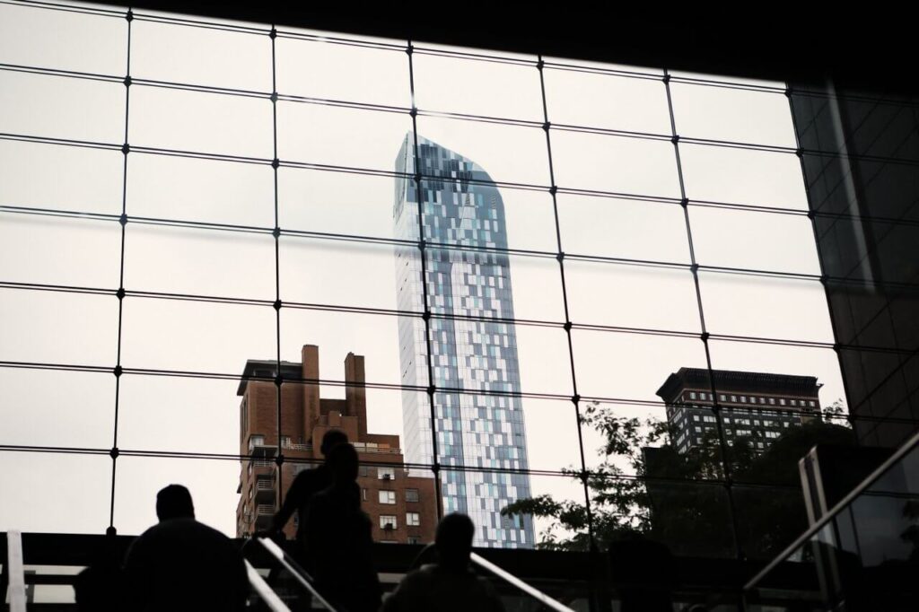Silhouetted people on stairs with a city skyline through large grid-like windows.