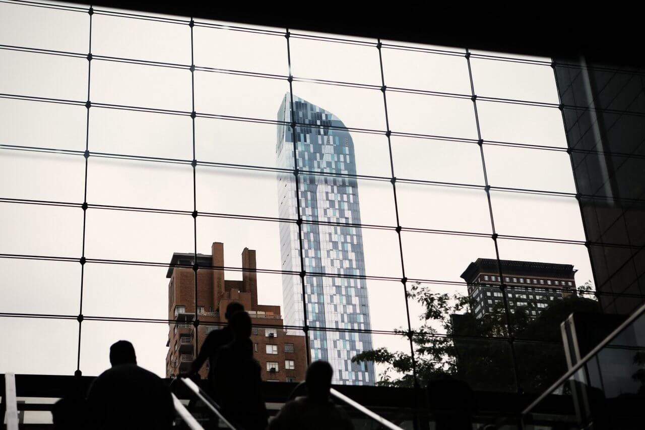 Silhouetted people on stairs with a city skyline through large grid-like windows.