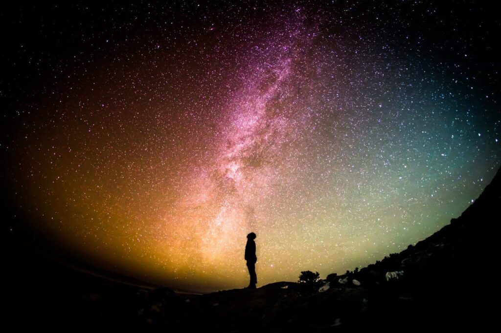 Silhouette of a person gazing at a vibrant, starry sky with the Milky Way overhead.