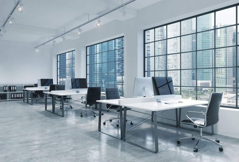 Modern open office with rows of white desks and chairs, large windows showcasing a city skyline.