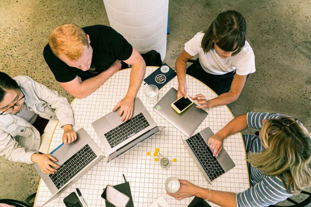 Group of four people working on laptops at a table, viewed from above.