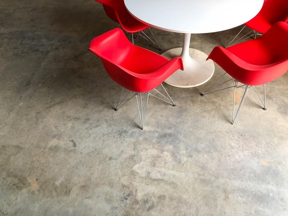 White round table with four red modern chairs on a concrete floor.