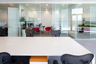 Modern office with a white conference table, black chairs, glass walls, and a distant red chair.