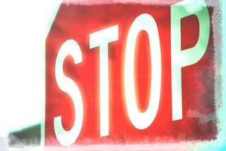 Close-up of a red stop sign with white text, viewed from a low angle and slightly faded edges.