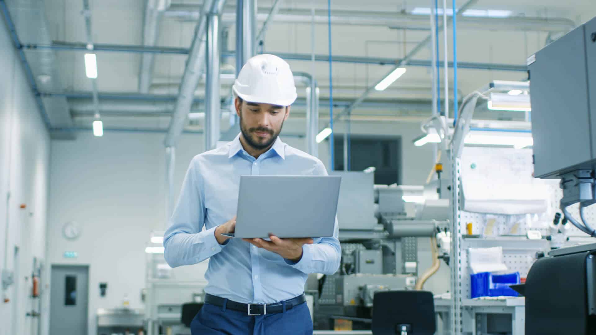 Man in a hard hat using a laptop in an industrial setting.