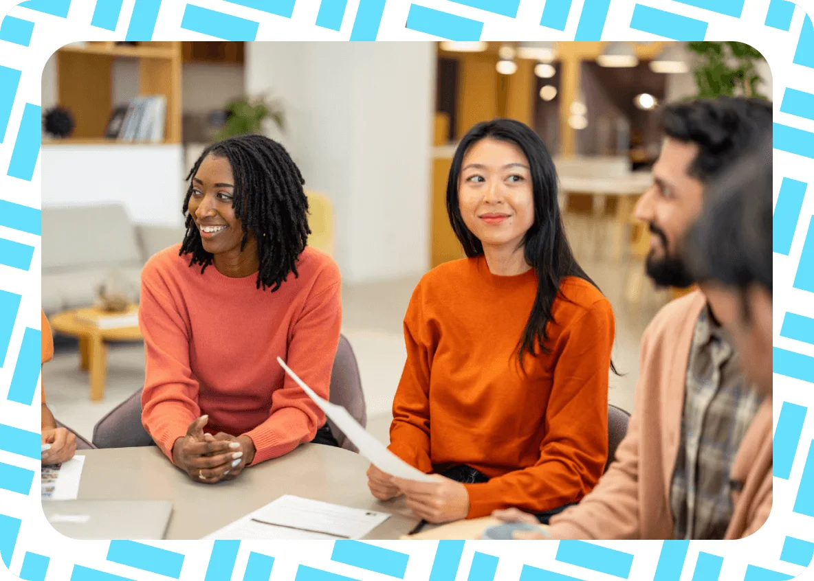 Three people sit at a table having a discussion in a modern office. Two women and one man are smiling, with papers—including what appears to be a market report—and a laptop in front of them. The image has a blue border with a white geometric pattern.