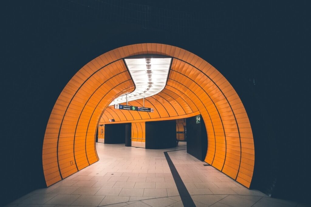 A modern, brightly lit orange tunnel with a curved design in a subway station.