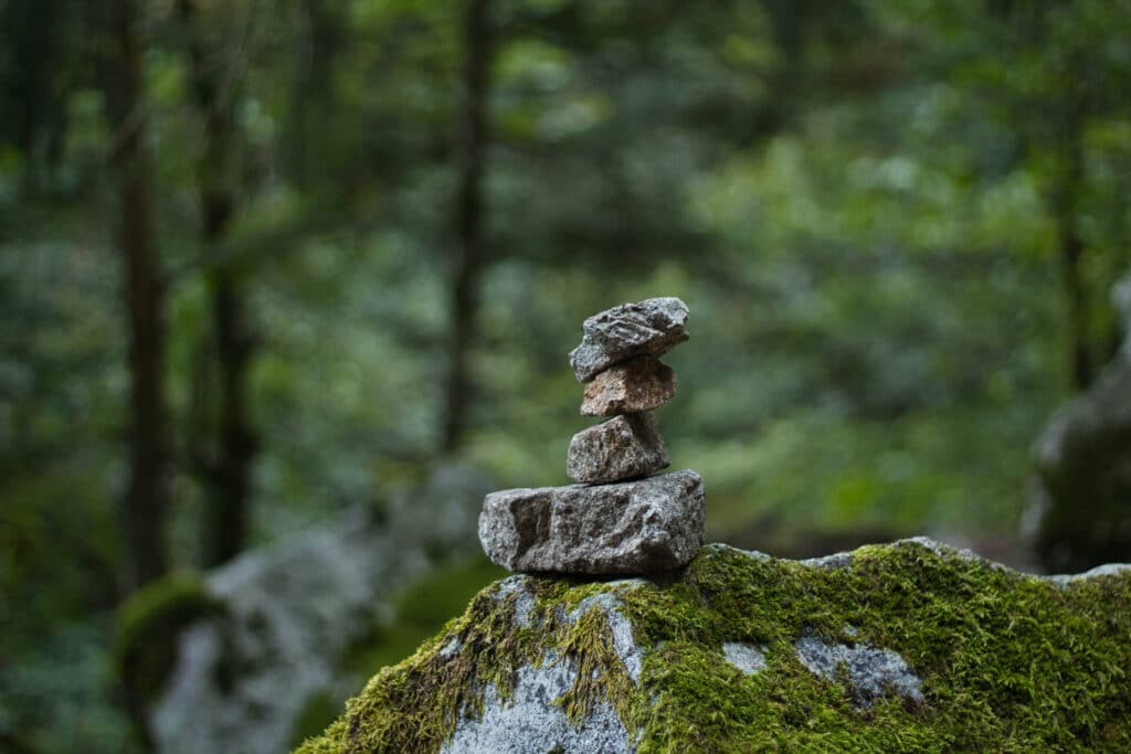 Balanced stones on a moss-covered rock with a blurred forest background.