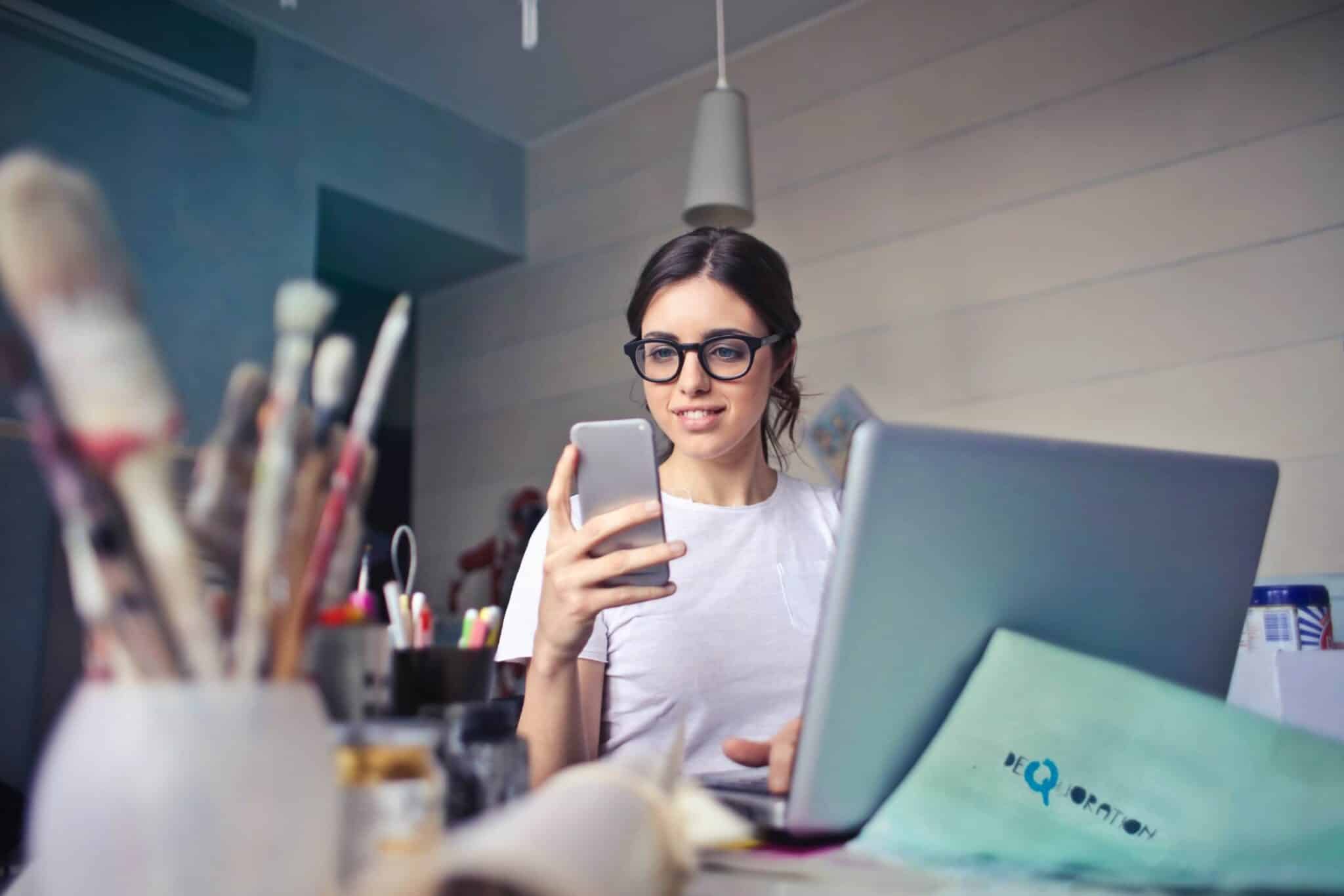 woman-in-white-t-shirt-holding-smartphone-in-front-of-laptop-914931